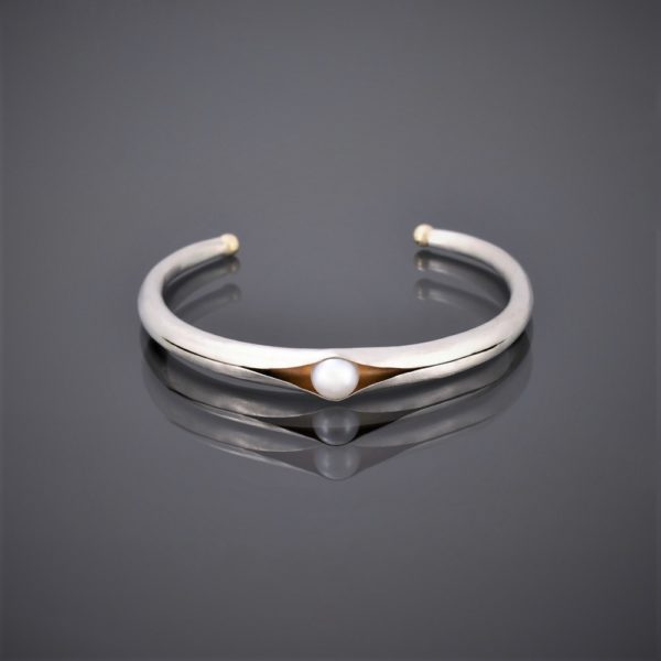 Horizontal view of folding anticlastic matt silver cuff holding a freshwater pearl. Gold detailing on tips
