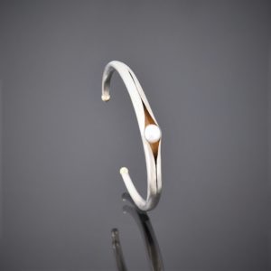Upright right view of anticlastic matt silver cuff holding a freshwater pearl. Gold detailing on tips