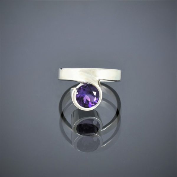 Front view of a wide silver ring with a facetted amethyst set in a rubover setting