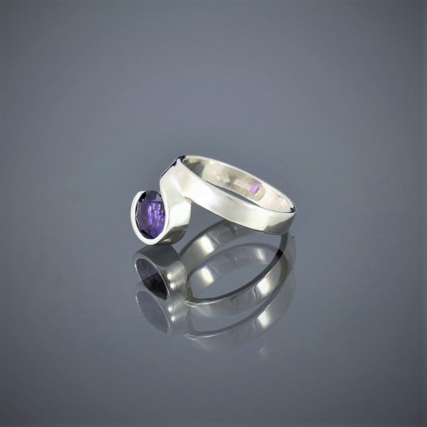 Left view of a wide silver ring with a facetted amethyst set in a rubover setting