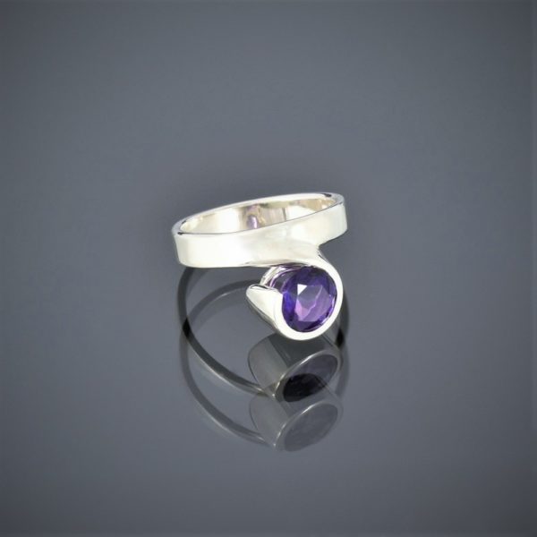 Right view of a wide silver ring with a facetted amethyst set in a rubover setting