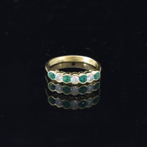 Front view of 18ct yellow gold ring with 7 alternated diamonds and emeralds on black background